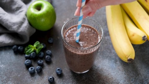 Healthy raw fruit and chocolate protein smoothie. Female hand stirring smoothie in glass with paper cocktail straw. Healthy fitness vegan lifestyle concept