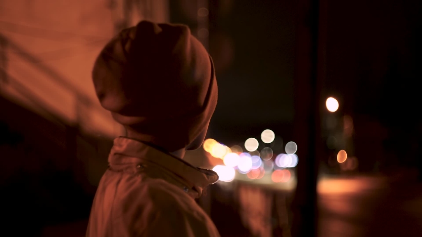 Boy in a jacket and hat stands on the night street. Homeless children. City lights Royalty-Free Stock Footage #1048020817