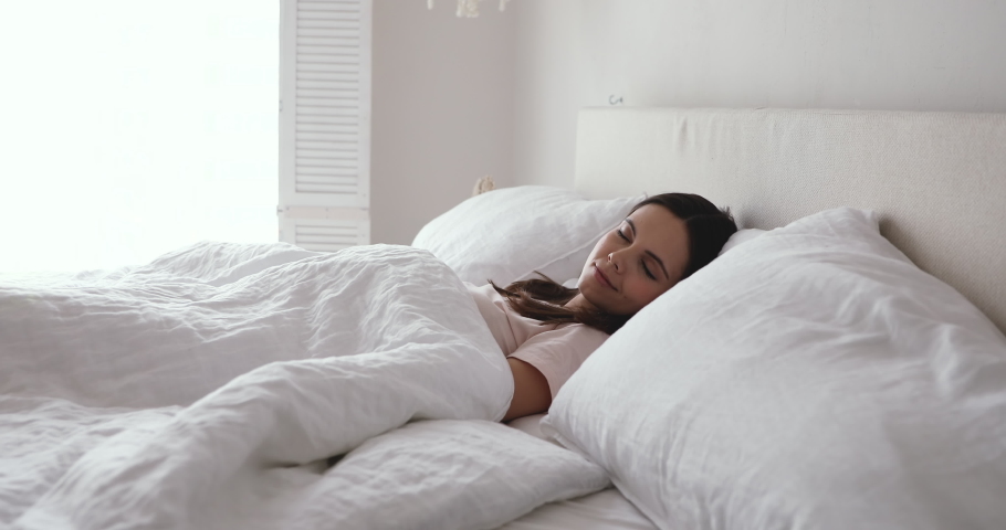 Happy sleepy young adult woman waking up lying in comfortable white bed. Positive pretty girl stretching enjoying early good morning in cozy bedroom. Fresh lazy lady awakes after healthy sleep at home Royalty-Free Stock Footage #1048023898