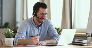 Smiling businessman wear wireless headset making conference video call on laptop. Male professional call center agent, hr manager having distance webcam chat job interview on computer in office.