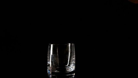 Whiskey pouring into glass isolated on black close up slow motion.