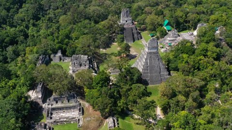 Aerial, tilt up, drone shot overlooking pyramid temples, in Guatemalan jungle, at the ancient Tikal city, on a sunny day, in Peten, Guatemala, Central America