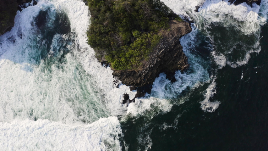 Scenic aerial view of big waves crash against small islands near coast