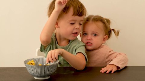 Brother and sister quarrel and fight. Cute little boy hits the girl on the arm and does not share breakfast cereals in morning at home