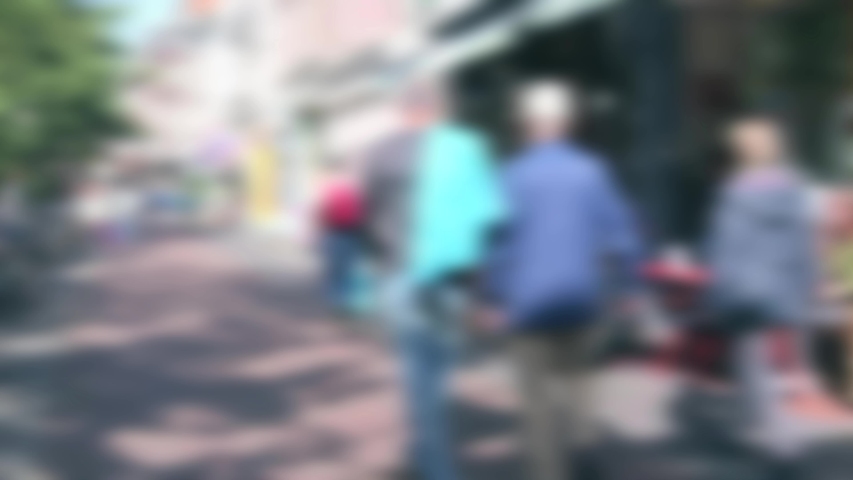 Abstract blurred people walking down an urban street in sunshine with parked bicycles on one side and cafe at the other.