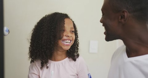 Side view close up of an African American man and his mixed race daughter enjoying time at home together, brushing teeth, making fun together, laughing, in slow motion