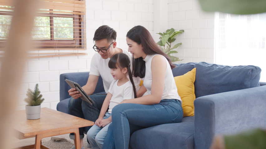 Slow motion wide shot : Happy warm family father, mother and daughter watching funny tv online on digital tablet computer sitting on couch together, parents with kids enjoying mobile apps on tablet