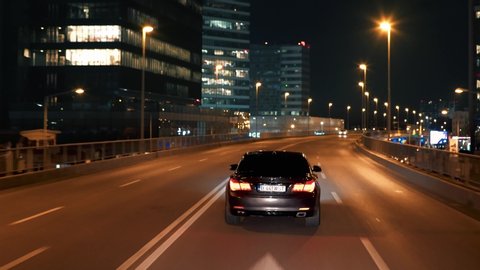 Bucharest, Romania - 02.20.2020: Crane rolling shot of a BMW 7 Series luxury sedan car driving on a city bridge at night with skyline view 