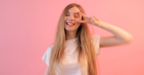 Portrait of a cheerful, playful girl dressed in a white t-shirt , gesturing like a v-shaped sign next to a winking eye, showing her tongue and looking at the camera