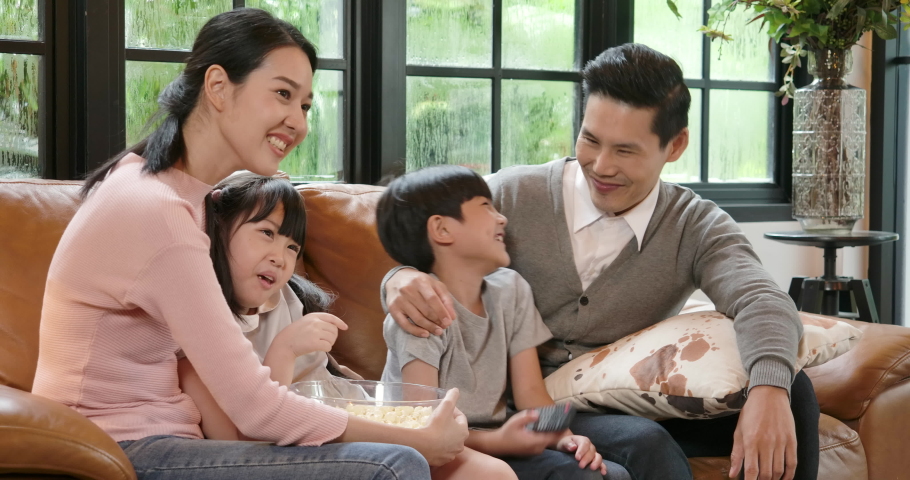 Happy family watching tv together at home. Cheerful young asian parents and cute small kids enjoy television together on sofa having fun in living room at home.