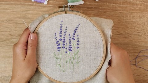 Woman makes embroidery a beautiful picture of lavender flowers. Handmade craft embroidery. Embroidery with a wooden hoop in the art of craft technique with a flower