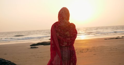 Young women wearing a red saree on the beach goa India.girl in traditional indian sari on the shore of a paradise island among the rocks and sand enjoying the freedom and the sunset