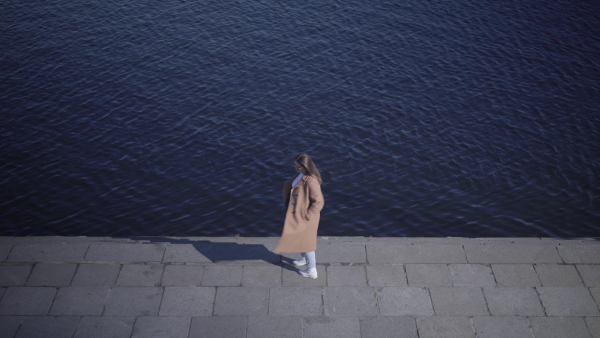 Top view of cheerful Caucasian young woman spinning on river bank. Wide shot of happy chubby girl enjoying sunny day outdoors. Happiness, lifestyle, joy, leisure.