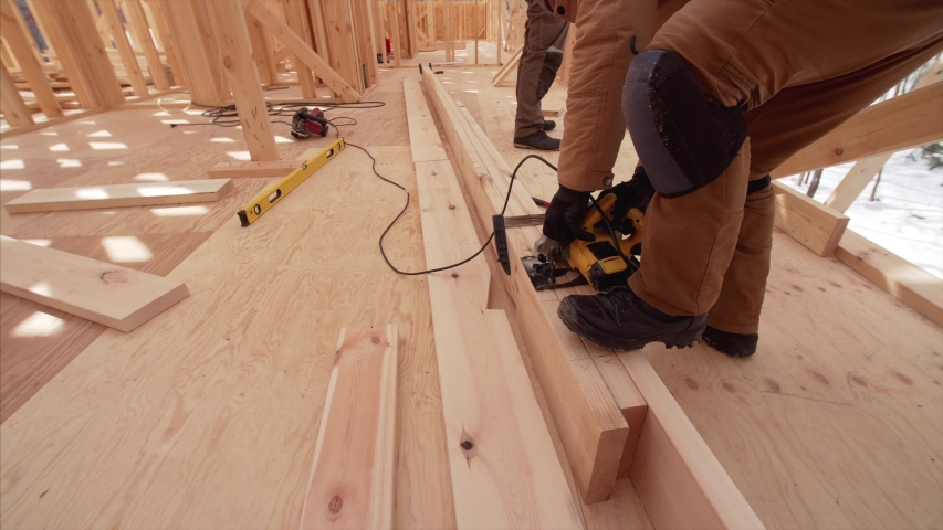 Builder in gloves is cutting three wooden planks with small electric circular saw. Frame house building | Shutterstock HD Video #1048087612
