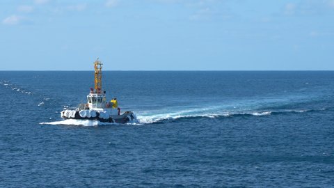 A new bright, powerful sea tugboat swims quickly across the blue waves of the ocean on a sunny day. Japanese tugboat escorts the ship to the port. sea ​​foam