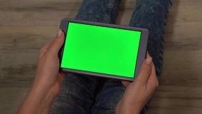 Closeup point of view video of woman sitting on wooden floor and looking at empty green screen of modern mobile tablet pc