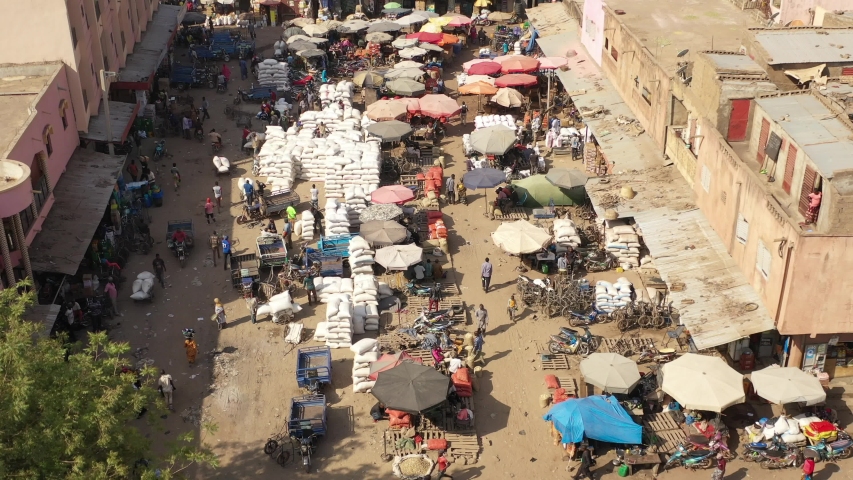 The drone flies over with a tilt downwards a buzzing and crowed street with trucks, scooters, people and sandbags in the midst of the city in Mali Aerial Drone Footage 4K Royalty-Free Stock Footage #1048112377