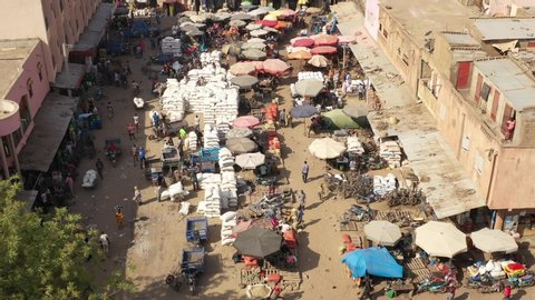The drone flies over with a tilt downwards a buzzing and crowed street with trucks, scooters, people and sandbags in the midst of the city in Mali Aerial Drone Footage 4K