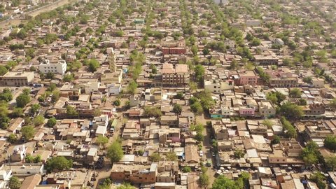 The drone flies with a turn towards the left with a slight tilt downwards a village surrounded by vegetation and sandy roads in Mali Aerial Drone Footage 4K