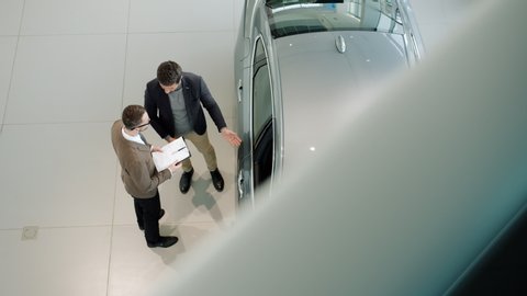 Sales manager is opening car door and inviting male customer to see the auto inside while buyer is choosing automobile in dealership. People and business concept.