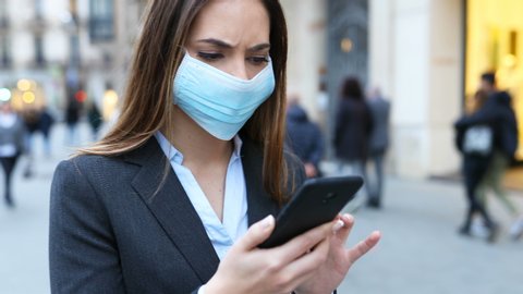 Worried executive wearing mask walking checking news on smart phone