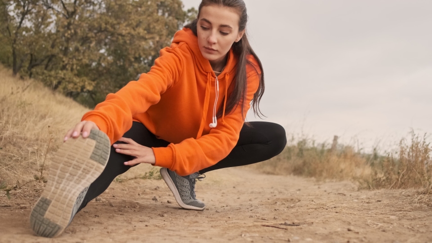 Concentrated pretty athletic woman in earphones warming up with legs at seashore Royalty-Free Stock Footage #1048124788