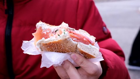 Close up of man holding a bagel with cream cheese, smoked salmon, tomato, onion, and capers