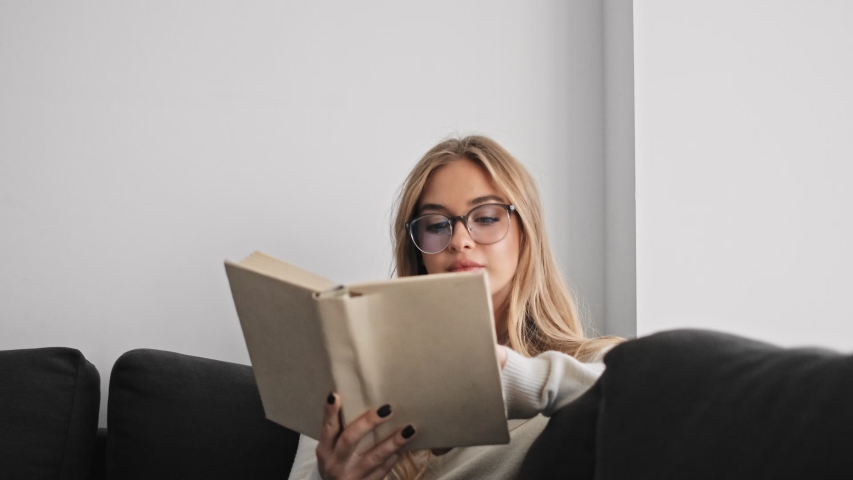 A beautiful young woman is reading a book while sitting in the living room