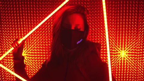 UFA/RUSSIA - 02.03.2020: Young beautiful girl model in neon lights. Neon triangle in a club studio. Concept of dubstep or punk style. Model in a red neon studio. Wearing a medical black mask