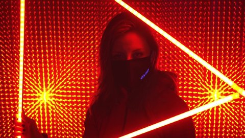 UFA/RUSSIA - 02.03.2020: Young beautiful girl model in neon lights. Neon triangle in a club studio. Concept of dubstep or punk style. Model in a red neon studio. Wearing a medical black mask