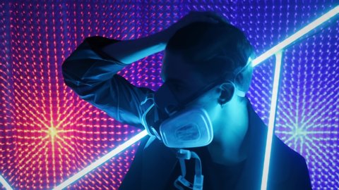 A model guy is dancing in a neon studio in a gas mask. Concept in dubstep style. Air pollution and global warming. Rave party