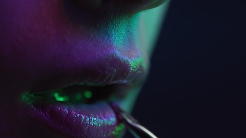 Young Woman Applying Lipstick on Lips. Cosmetics for Make-Up and Gloss of Posing Girl in Multi-Colour Neon. Flickering Rainbow of Lighting at Fashion Studio. Shot of Modern Makeup on Black Background