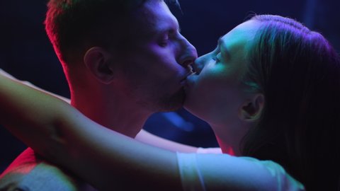 Two Lovers Hugging and Kissing in Colourful UV Light of Urban Street. Intimacy of Pretty Couple in Multi-Colour Filter of Dark Room Indoors. Modern Love of Young Pair in Iridescent Shine of Neon Sign