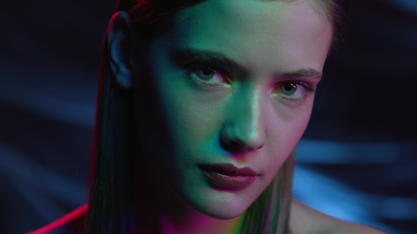 Portrait of Girl Looking at Camera in Colourful Filter. Multi-Colours in Neon Lighting of Dark Room. Futuristic Advertisement of Fashion with Young Woman. Lady Watching on Ultra-Violet Light of Night