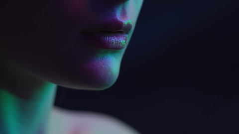 Lips of Woman in Colourful Neon Lighting. Beauty of Female Face in Flickering Multi-Colours Indoors. Make-Up Advertisement in Room with Black Background. Fashion Makeup on Skin of Charming Young Girl