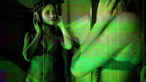 Scratched vintage celluloid film of a young woman reflected in mirror wearing a bra and headphones and looking at the camera