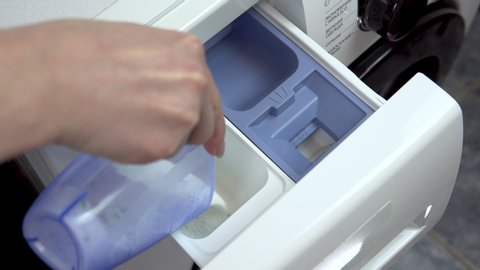 A young woman pours detergent into a washing machine. A woman fills powder and pours liquid into a special compartment in the washing machine. Hand close-up.