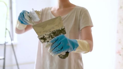 Young female worker preparing putty for the wall repair. Close-up video of spreading plaster on metal spatula.