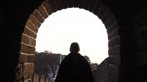 Happy woman walk at Great Wall of China, come down from watch tower at Badaling section at sunset in winter. Travel concept