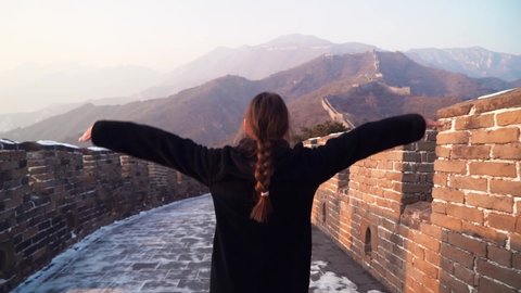 Happy woman walk at Great Wall of China, come down from watch tower at Badaling section at sunset in winter. Travel concept. Follow shot