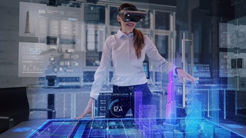 Professional Female Architect wearing Augmented Reality Holo Lens makes gestures and redesigns 3D City Model. High Tech Office use Virtual Reality Holographic Modeling Software Application.