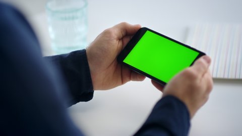 Close up man hands holding smartphone with green screen. Unrecognized business man reading message on mobile phone with chroma key. Male professional looking cell phone screen in slow motion.