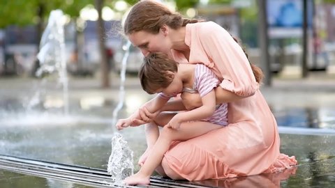 Portrait of beautiful disabled girl in the arms of his mother having fun in fountain of public park at sunny summer day. Child cerebral palsy. Inclusion.