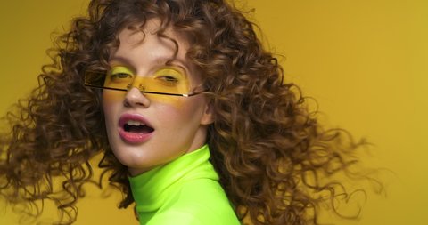 Fashion Video Shot of Attractive Creative female Model with Bright Makeup and stylish Eyeglasses. Looking pretty and having neon Top. Woman with curly Afro Hairstyle and Nice Appearance. Slow motion.