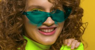 Young Beautiful Woman showing and Demonstrating Nice Bright Makeup in the Studio. Looking stylish with Trendy Eyeglasses and neon green Top. Yellow wall in the Background. Slow motion video.