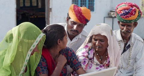 Young teenage daughter wither her mother, father and grand parents and teaches educates of portable laptop- dressed in traditional costumes from Rajasthan India- colorful turban and salwar kameez
