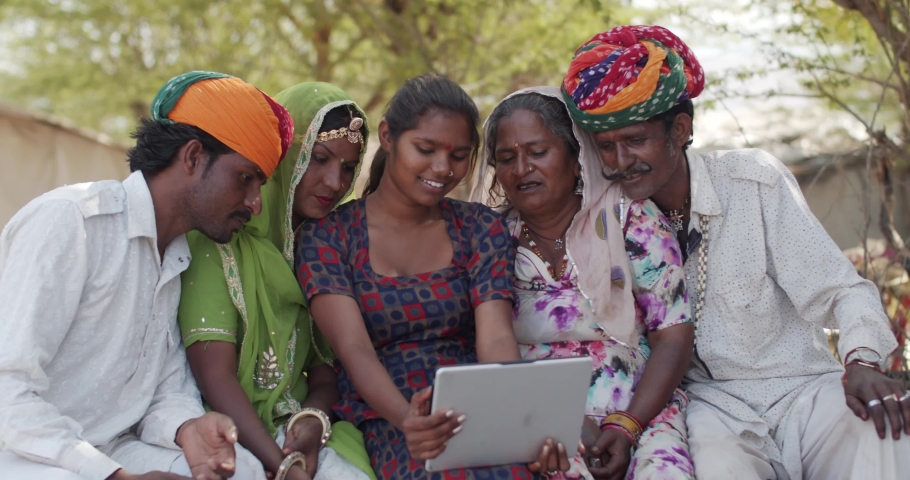 Three generations of a Rajasthani family, in traditional colorful costumes in India taking photo video selfies on a portable wifi tablet with touch screen in a rural setting exterior outdoors house