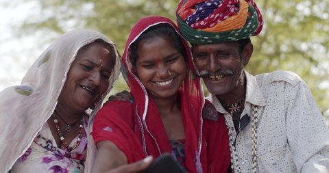 Pretty teenage girl teaches educates explains her grandparents to use a smart phone mobile handy device to take selfie photo video and then review them video chat con-call in rural India outdoors