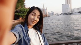 Attractive of asian woman taking selfie video chat with her friends sharing enjoyment vacation summer traveling in Bangkok Thailand while standing beside Chao Phraya River in Thailand.