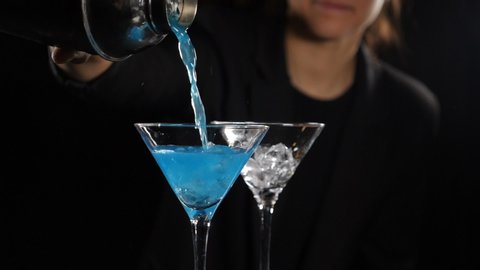 Female bartender preparing bright blue cocktail pouring liquid out of shaker. Making alcoholic cocktail with ice. Barmaid making cocktail in slow motion. Full hd